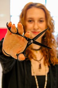 A young woman is holding a black pair of cutting shears towards the camera.